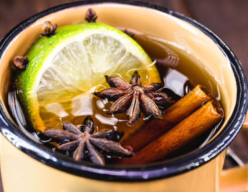 Descubra como fazer quentão para sua festa junina 2 Xícara com quentão, anil estrelado, canela em pau e rodela de limão.