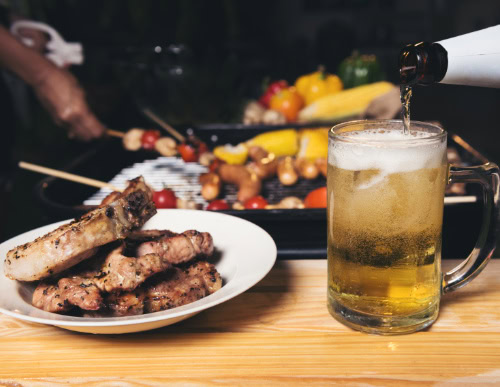 Copa do Mundo e churrasco: como fazer uma celebração de sucesso 2 Mesa com chopp e prato com carne, e churrasqueira ao fundo.