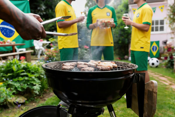 Copa do Mundo e churrasco: como fazer uma celebração de sucesso 7 Churrasqueira e pessoas com roupa da seleção brasileira ao fundo.