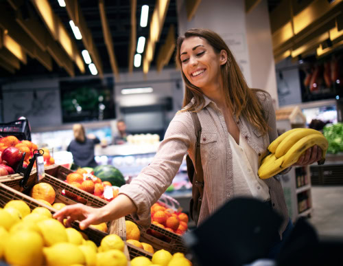 Descubra como economizar no supermercado com planejamento e estratégia 2 Mulher escolhendo frutas no hortifrúti.